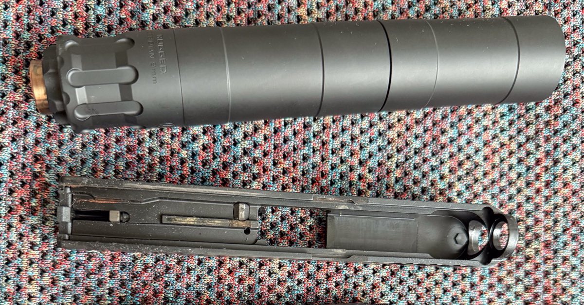 Rugged Obsidian 9mm suppressor beside a disassembled Glock slide on a patterned cloth surface.